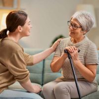 aide soignante discute avec une vielle femme avec une canne à son domicile