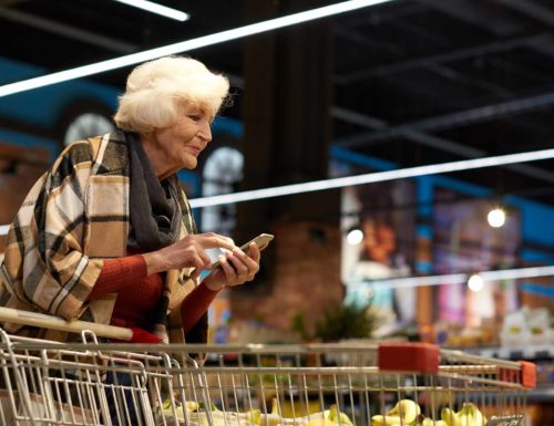 Vieille femme utile un smartphone au supermarché